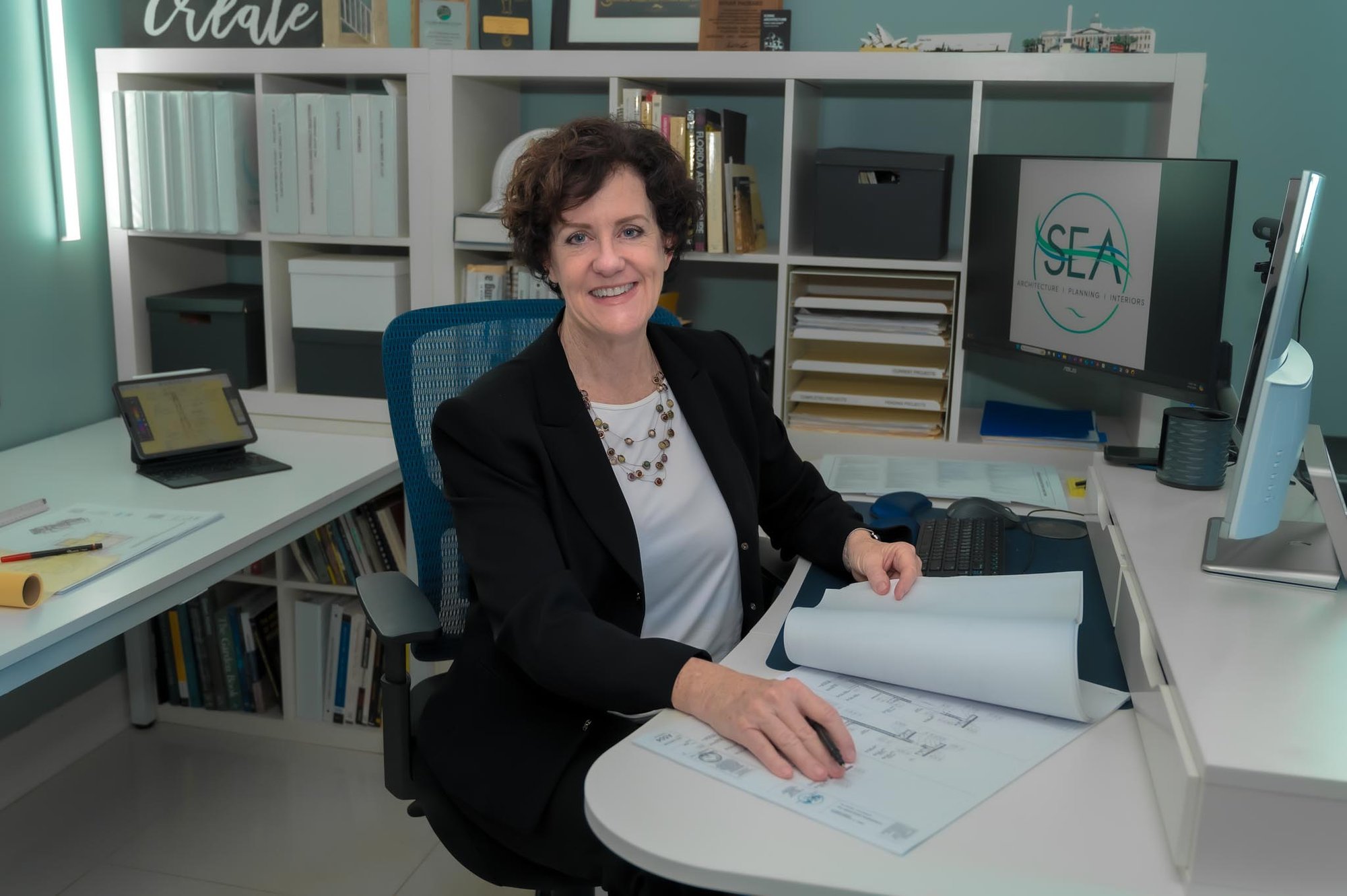 Susan - Headshots - Sitting at desk with logo