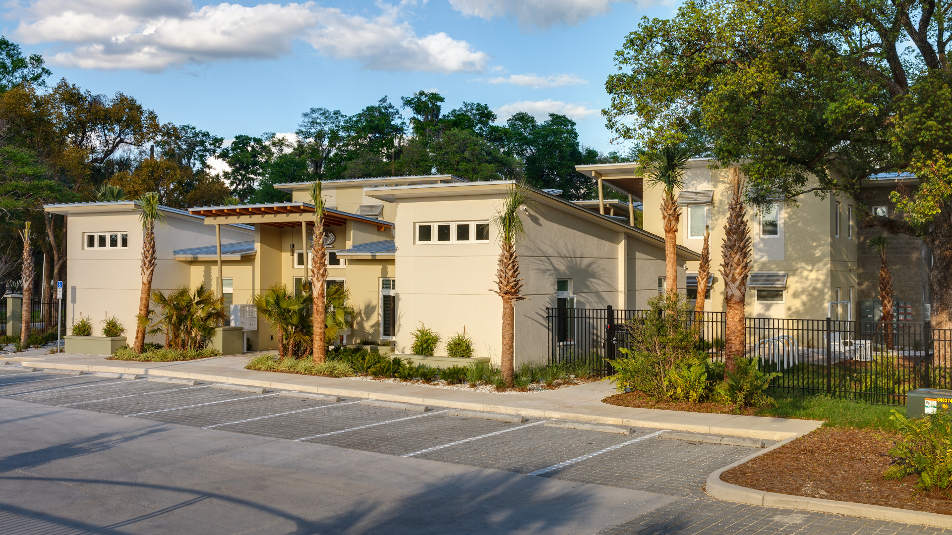 Image of eco-friendly designed apartment complex with sloped roofs, modern square windows, and palm tree landscaping